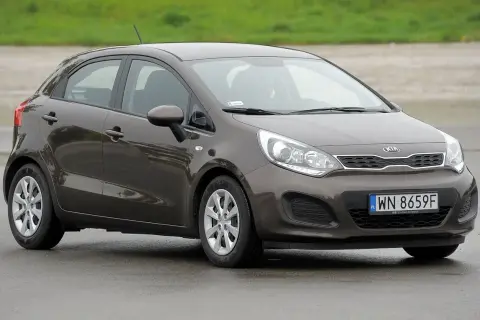 Brązowe kia rio 3 na mokrej nawierzchni, z widocznym numerem rejestracyjnym WN 8659F.