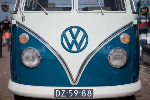 Przód klasycznego VW T2 w kolorze białym i niebieskim. Charakterystyczne okrągłe logo VW i okrągłe reflektory.