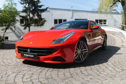 Czerwone Ferrari FF na brukowanej drodze, z widocznym logo Centrum.