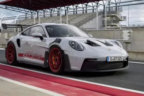 Biały Porsche 992 GT3 RS z czerwonymi akcentami i felgami pędzi po torze wyścigowym.