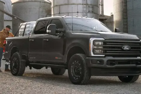 Mężczyzna ładuje pakunki do ciemnoszarego Forda Super Duty. Ciężarówka stoi na żwirowej drodze obok silosów.