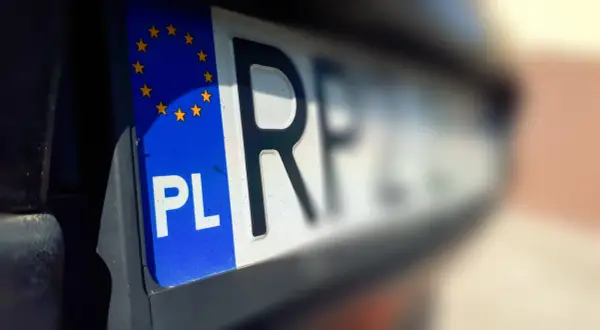 Zbliżenie na polską tablicę rejestracyjną z symbolem Unii Europejskiej. Litery "PL" i fragment kolejnych znaków są wyraźne, reszta rozmyta.