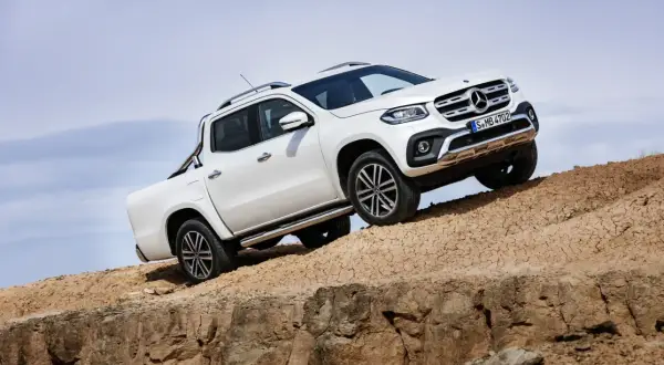 Biały mercedes pickup zjeżdża po piaszczystym zboczu, demonstrując swoje możliwości terenowe.