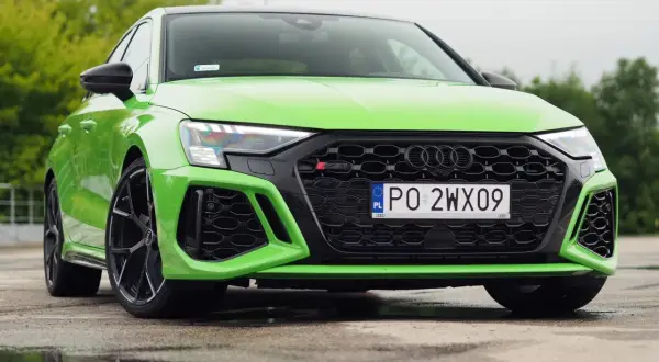 Jaskrawozielone Audi RS3 Sedan z czarnymi felgami stoi na mokrej nawierzchni, odbijając się w kałużach.