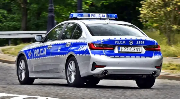 Srebrny radiowóz policyjny z niebieskimi pasami i napisem "POLICJA" na drzwiach i tyle. Widoczna tablica rejestracyjna HPZ C341.