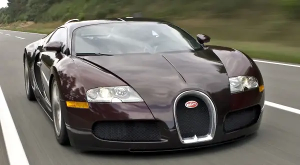 Ciemnobrązowy Bugatti Veyron pędzi po drodze. Jego cena jest astronomiczna, ale osiągi zapierają dech w piersiach.