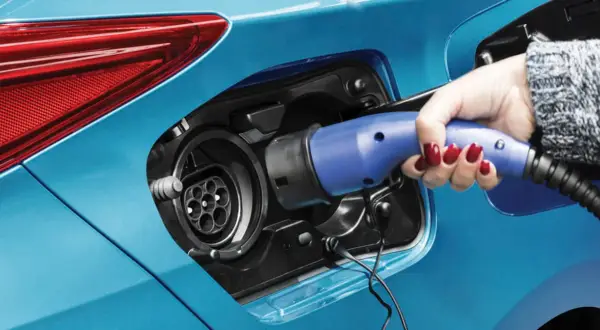 Dłoń z czerwonym lakierem na paznokciach podłącza ładowarkę do niebieskiej hybrydy plug-in.