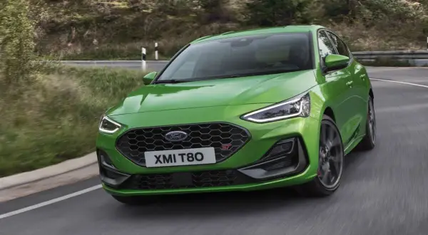 Jaskrawozielony Ford Focus 2025 ST z charakterystycznym grillem i światłami LED pokonuje zakręt na malowniczej, leśnej drodze.