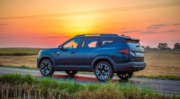 Ciemnoniebieska Dacia 4x4 na tle zachodzącego słońca, na polnej drodze.