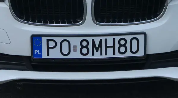 Biała maska samochodu z widocznym fragmentem kratki i tablicą rejestracyjną PO 8MH80.