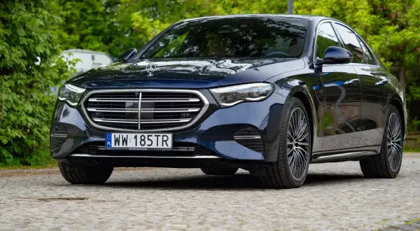 Elegancki, ciemnogranatowy Mercedes e300 lśni po deszczu na tle zieleni.