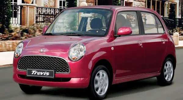 Czerwony Daihatsu Trevis z charakterystycznym grillem i okrągłymi światłami mija elegancki budynek.