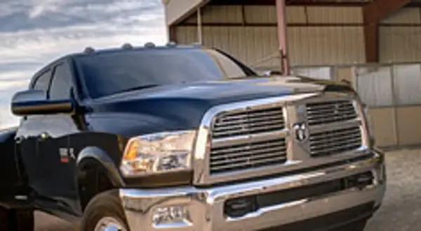 Ciemny Dodge Ram 3500 z chromowanym grillem i błyszczącym lakierem stoi przed budynkiem.