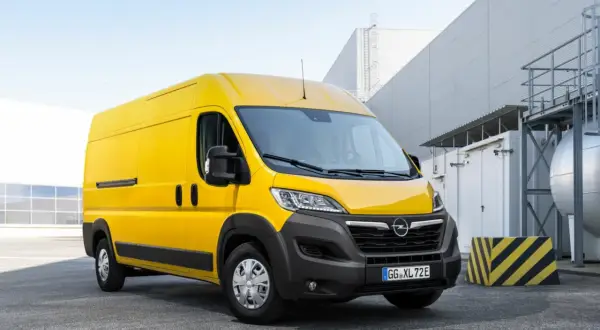 Żółty Opel Movano stoi na parkingu przed nowoczesnym budynkiem przemysłowym.