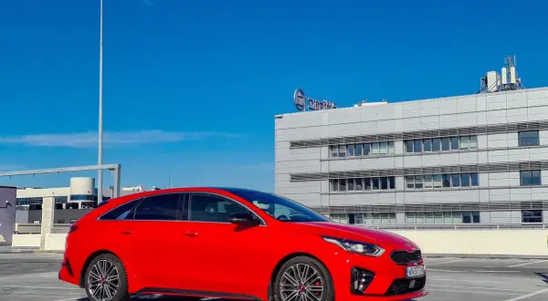 Czerwony Kia Proceed GT na parkingu pod nowoczesnym budynkiem.