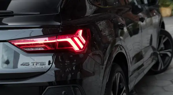 Czarne Audi Q3 45 TFSI quattro z zapalonymi światłami LED. Zbliżenie na tylną część pojazdu, podkreślające jego sportowy charakter i wymiary.