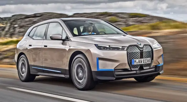 Elegancki suv BMW iX jedzie drogą wśród skalistych wzgórz.