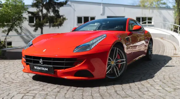 Czerwone Ferrari FF na brukowanej drodze, z widocznym logo Centrum.