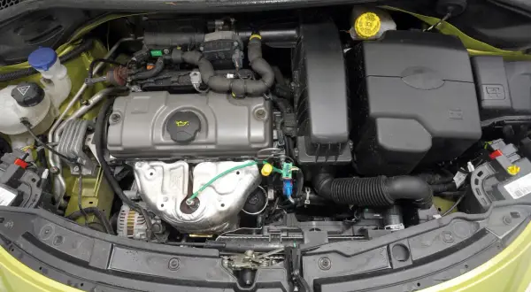 Silnik peugeot 207 1.4 benzyna. Widok komory silnika z widocznymi elementami, takimi jak alternator, obudowa filtra powietrza i zbiorniczek płynu chłodniczego.