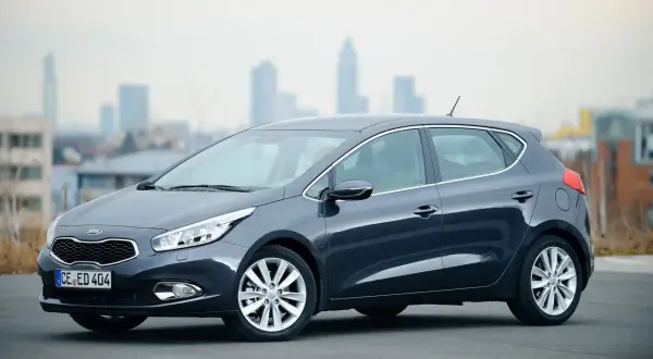 Ciemnoszary Kia Ceed 1.6 CRDi z eleganckimi felgami stoi na tle miejskiej panoramy.