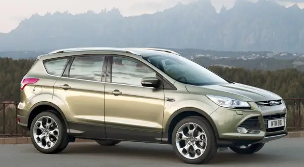 Złoty Ford Kuga na tle górskich krajobrazów. Wiele osób chwali ten model, a jego opinie są pozytywne.