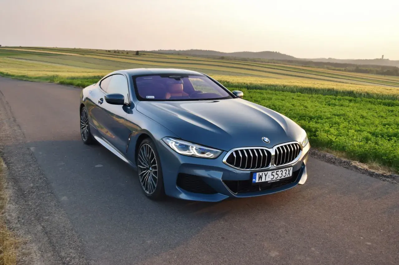 Niebieskie BMW 840d na tle pól zbożowych o zachodzie słońca.