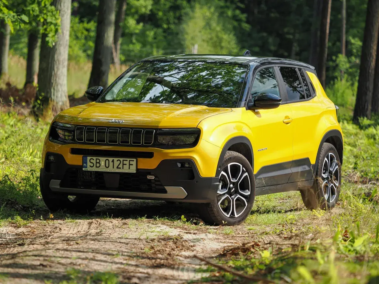 Żółty Jeep Avenger na leśnej drodze. Wiele pozytywnych jeep avenger opinie potwierdza jego miejski charakter i stylowy wygląd.