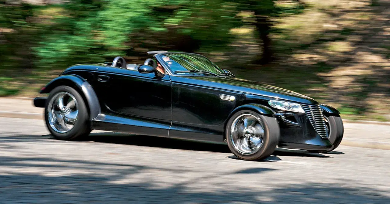 Czarny Plymouth Prowler z opuszczonym dachem pędzi po krętej drodze, otoczony rozmazaną zielenią drzew.