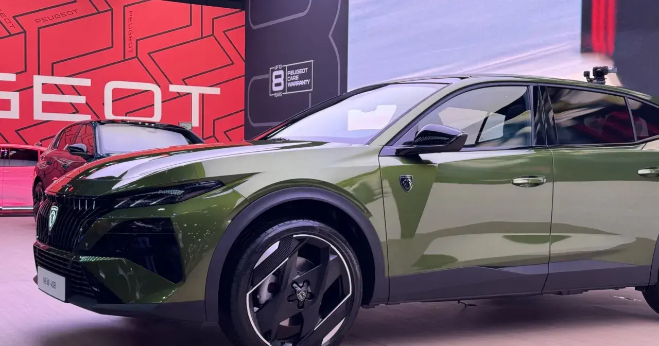 Nowy Peugeot 408 Hybrid w kolorze oliwkowym prezentuje się nowocześnie. Z przodu widoczny jest charakterystyczny grill i reflektory.