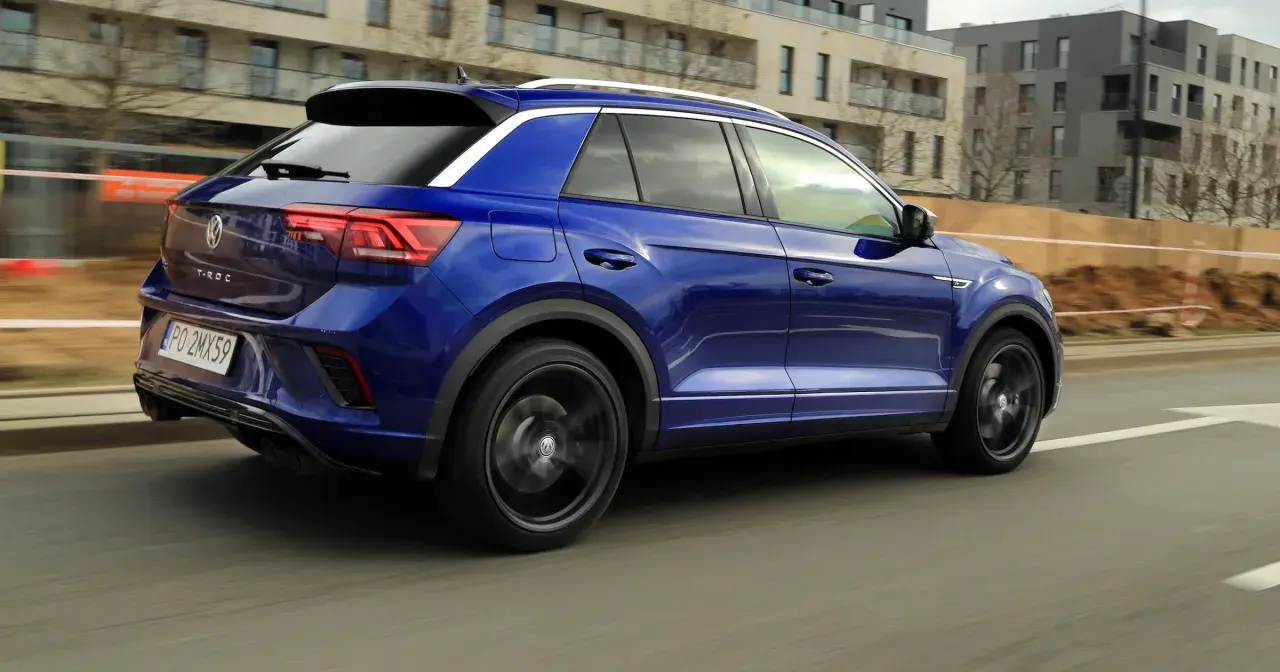Niebieski Volkswagen T-Roc pędzi ulicą. W tle nowoczesne budynki i plac budowy.