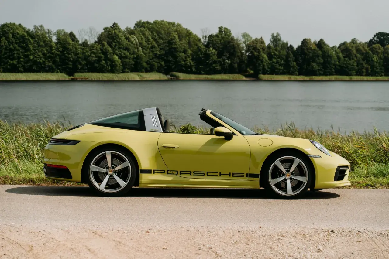 Żółty Porsche Targa z czarnym napisem na progu, zaparkowany nad jeziorem, otoczony zielenią.