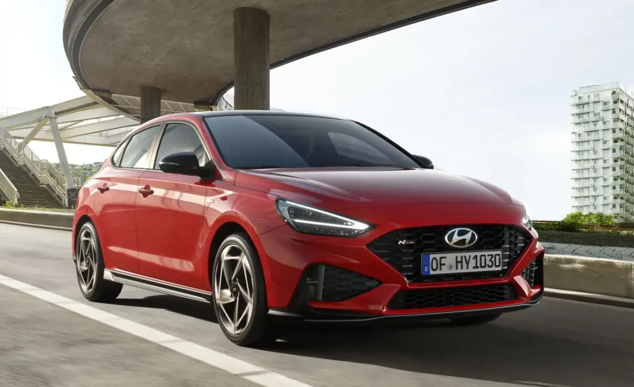 Czerwony Hyundai i30 hatchback N Line w ruchu miejskim, z nowoczesną architekturą w tle.