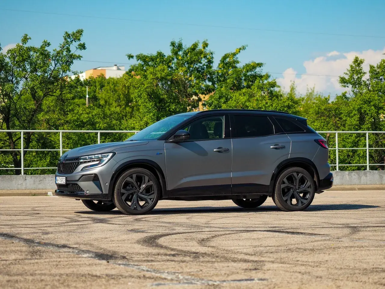 Szary Renault Austral na tle zieleni. Wiele osób szuka **Renault Austral opinie** przed zakupem.