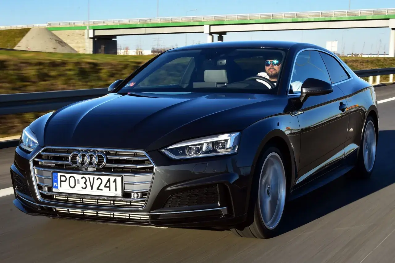Czarny Audi A5 na drodze. Kierowca w okularach przeciwsłonecznych. Wiele osób chwali audi a5 opinie.