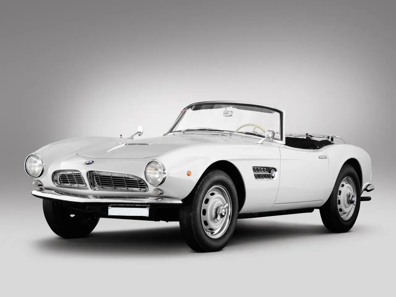 Biały kabriolet BMW 507 z lat 50. prezentuje się elegancko na szarym tle.