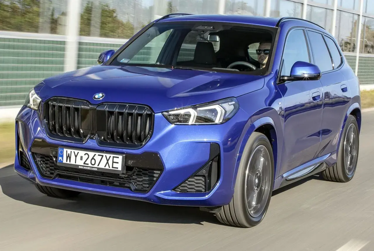 Niebieskie BMW X1 w ruchu, kierowca w okularach. Wiele osób szuka bmw x1 opinie przed zakupem.