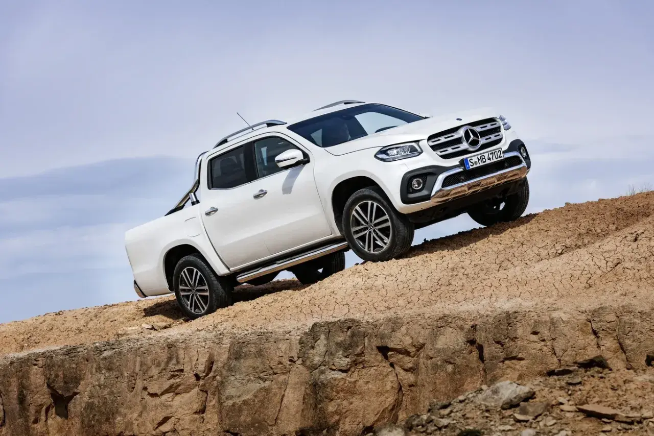 Biały mercedes pickup zjeżdża po piaszczystym zboczu, demonstrując swoje możliwości terenowe.