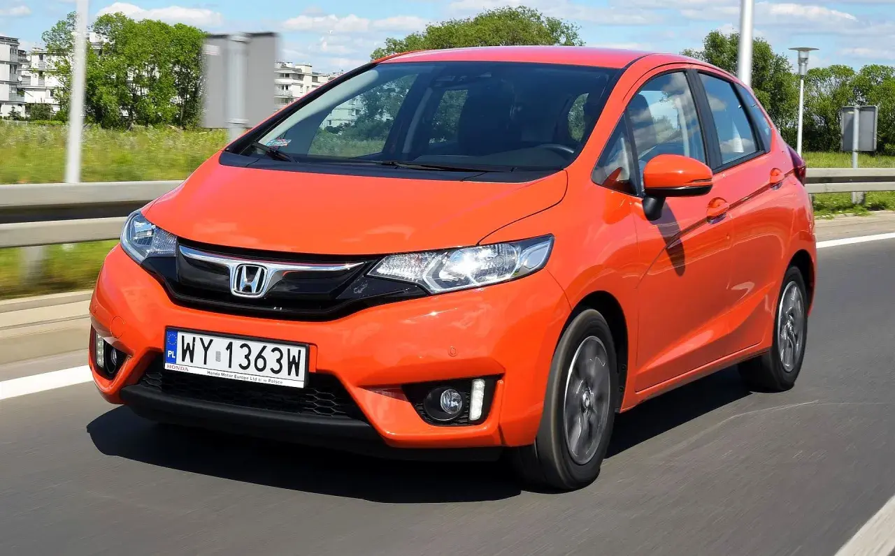 Pomarańczowy Honda Jazz w ruchu drogowym. Wiele osób szuka honda jazz opinie przed zakupem.