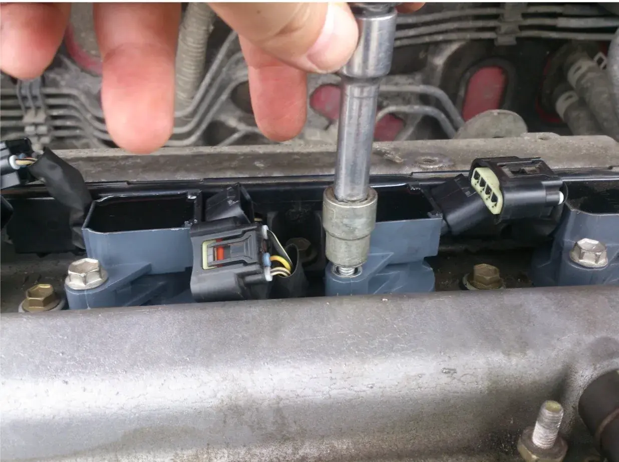 Naprawa Opla z błędem dtc p0301. Mechanik dokręca cewkę zapłonową kluczem nasadowym.