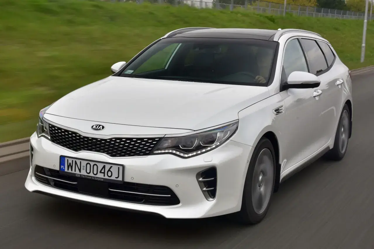 Biała Kia Optima w wersji kombi na drodze. Wiele pozytywnych kia optima opinie potwierdza jej wszechstronność.