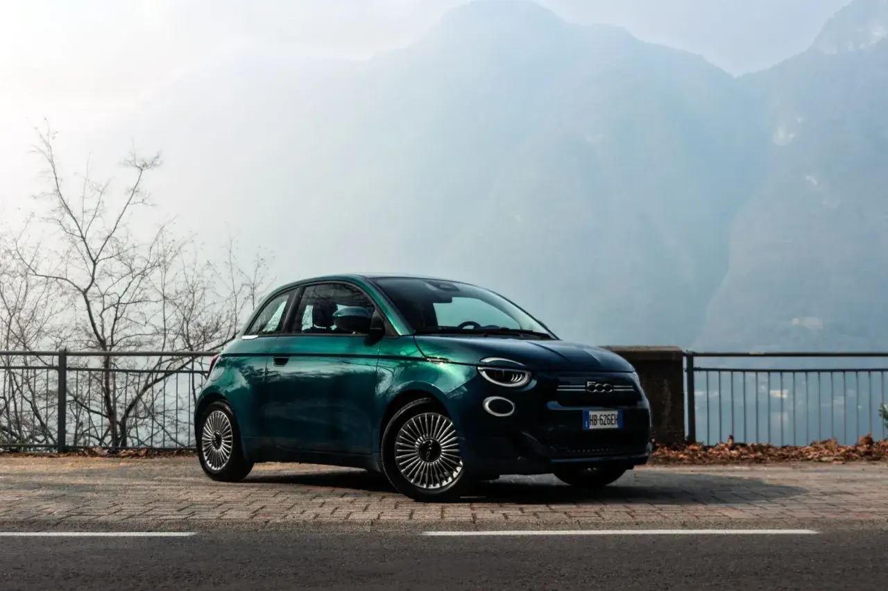 Zielony Fiat 500 na tle górskich krajobrazów. Wiele osób chwali ten model, a jego opinie są bardzo pozytywne.