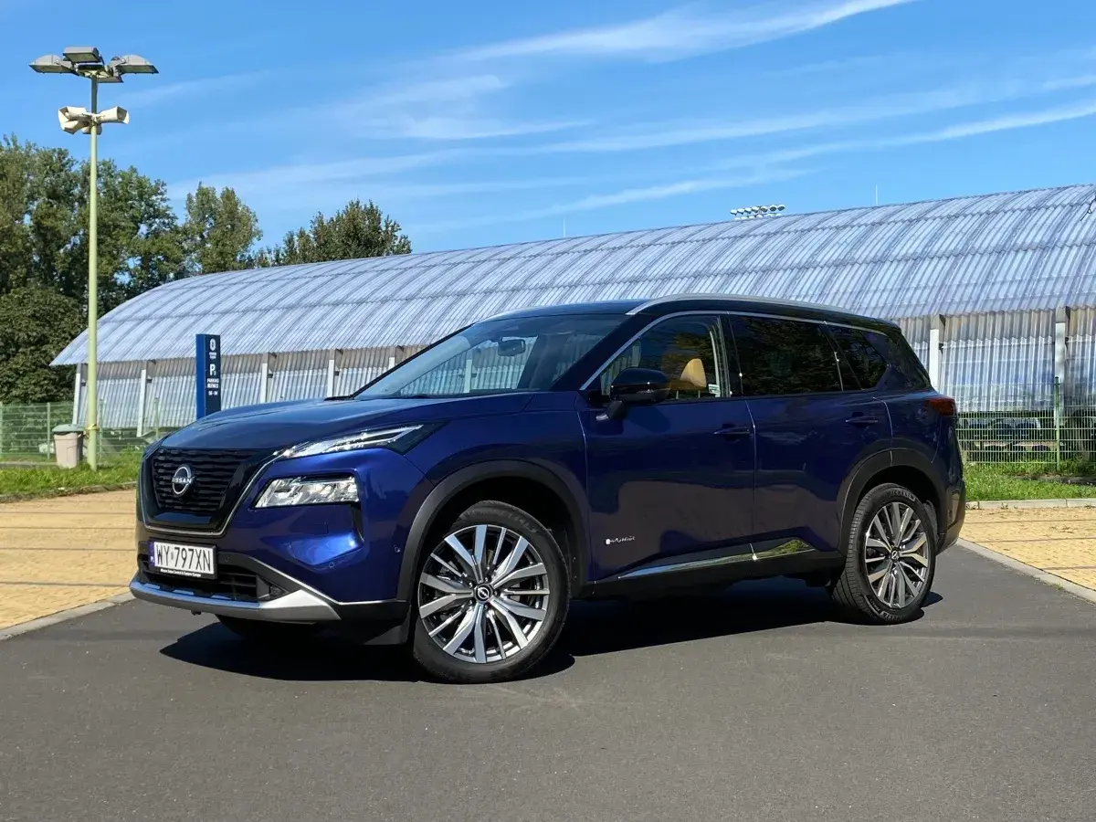 Niebieski Nissan X-Trail na tle hali sportowej. Wiele osób szuka nissan x trail opinie, ten SUV może być dobrym wyborem.