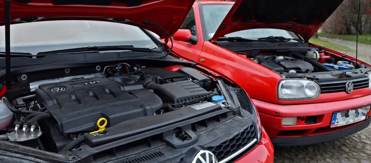 Dwa czerwone Volkswageny z otwartymi maskami. Silnik TDI w nowszym modelu, starszy model z przodu. Oba gotowe na paliwo diesel.