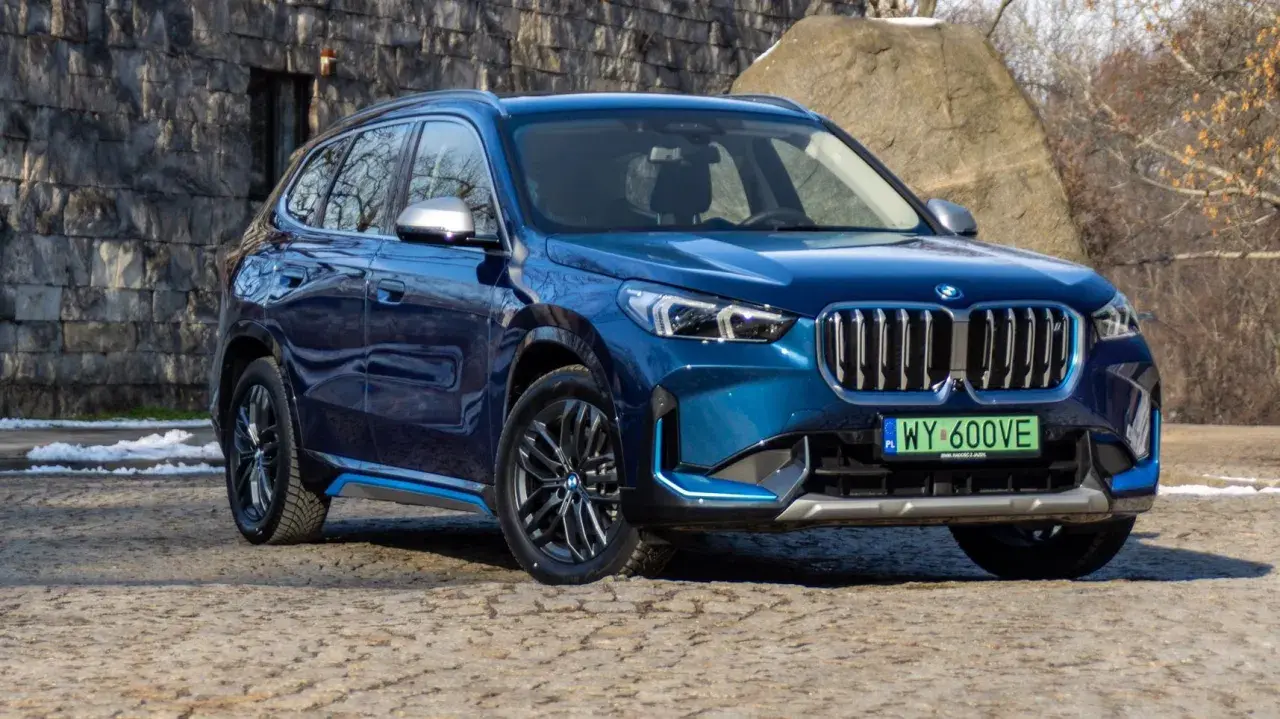 Błękitny BMW X1 elektryk z niebieskimi akcentami stoi na kamienistej drodze.