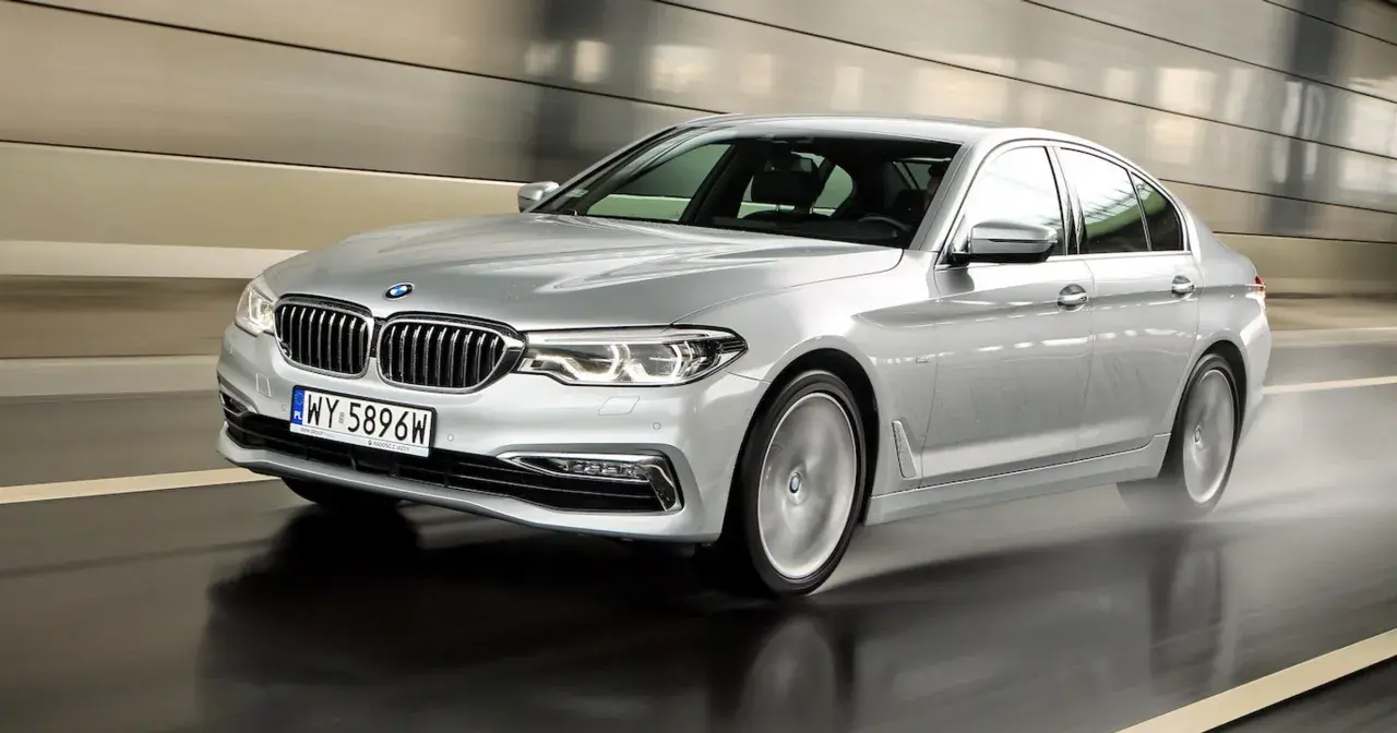 Srebrne BMW 520d xDrive w ruchu, z rozpryskującą się wodą spod kół, w nowoczesnym tunelu.