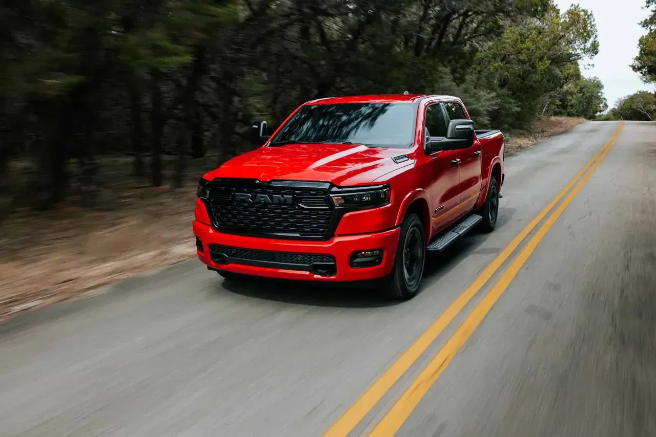 Czerwony Dodge Ram 1500 pędzi po krętej drodze wśród drzew.