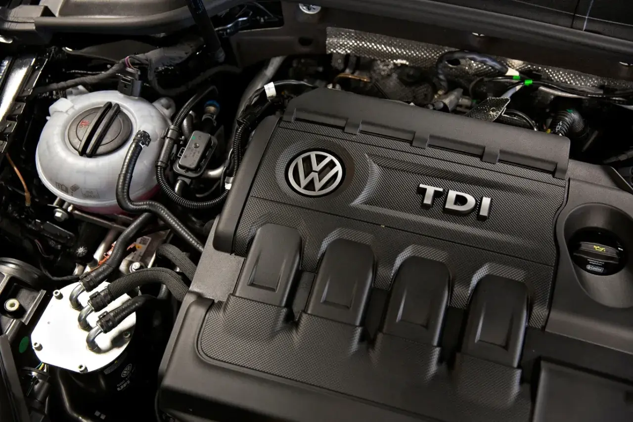 Silnik 2.0 TDI 140KM Volkswagena. Widoczny zbiornik płynu chłodniczego i osłona silnika z logo TDI.
