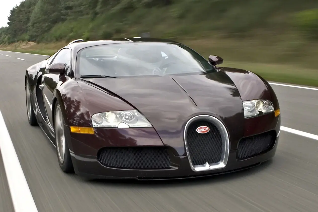 Ciemnobrązowy Bugatti Veyron pędzi po drodze. Jego cena jest astronomiczna, ale osiągi zapierają dech w piersiach.