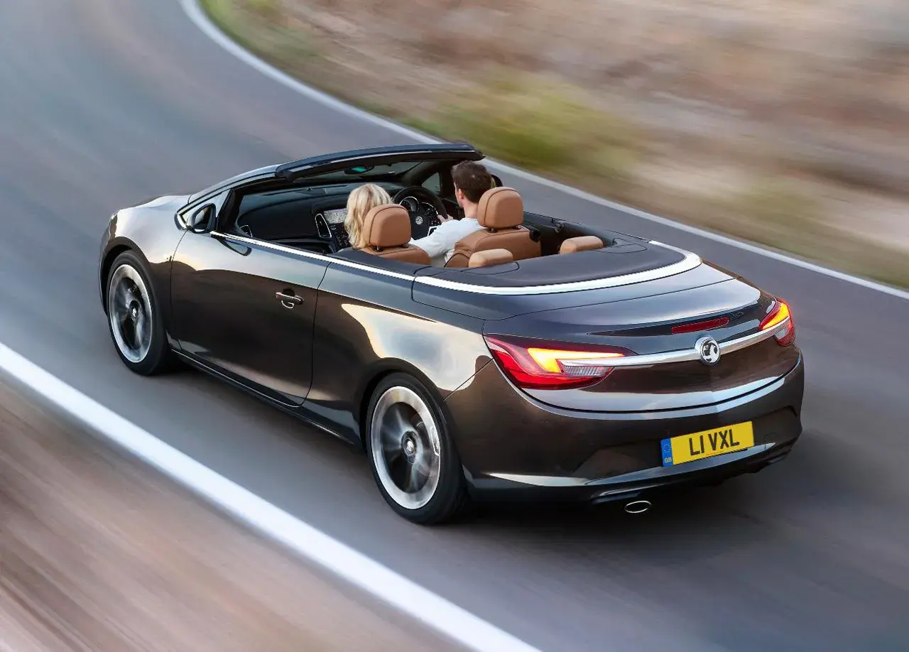 Para podróżuje lśniącym, ciemnobrązowym **Opel cabrio** po krętej drodze.