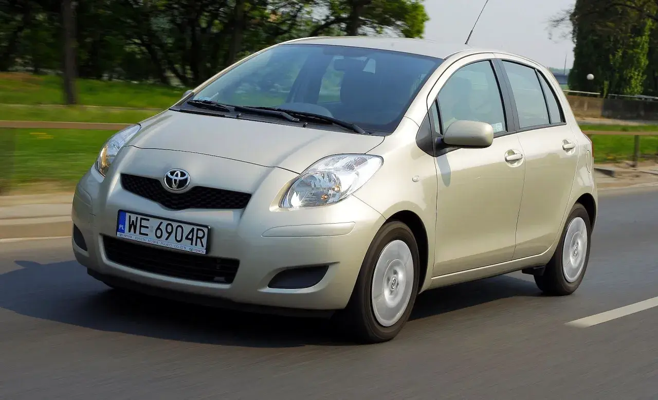Złoty Toyota Yaris 2006 na drodze, z zielenią w tle.